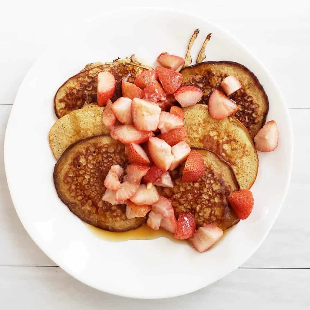 Banana oat pancakes on a plate topped with strawberries.