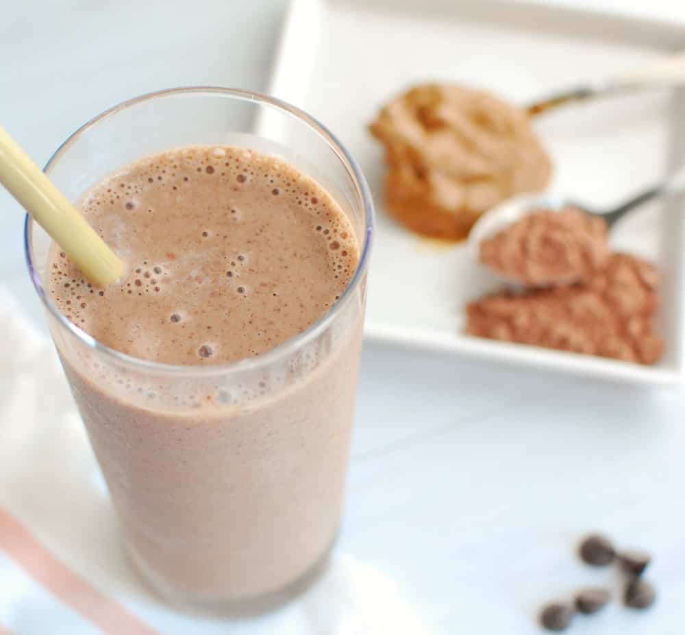 A chocolate smoothie next to some cocoa powder.