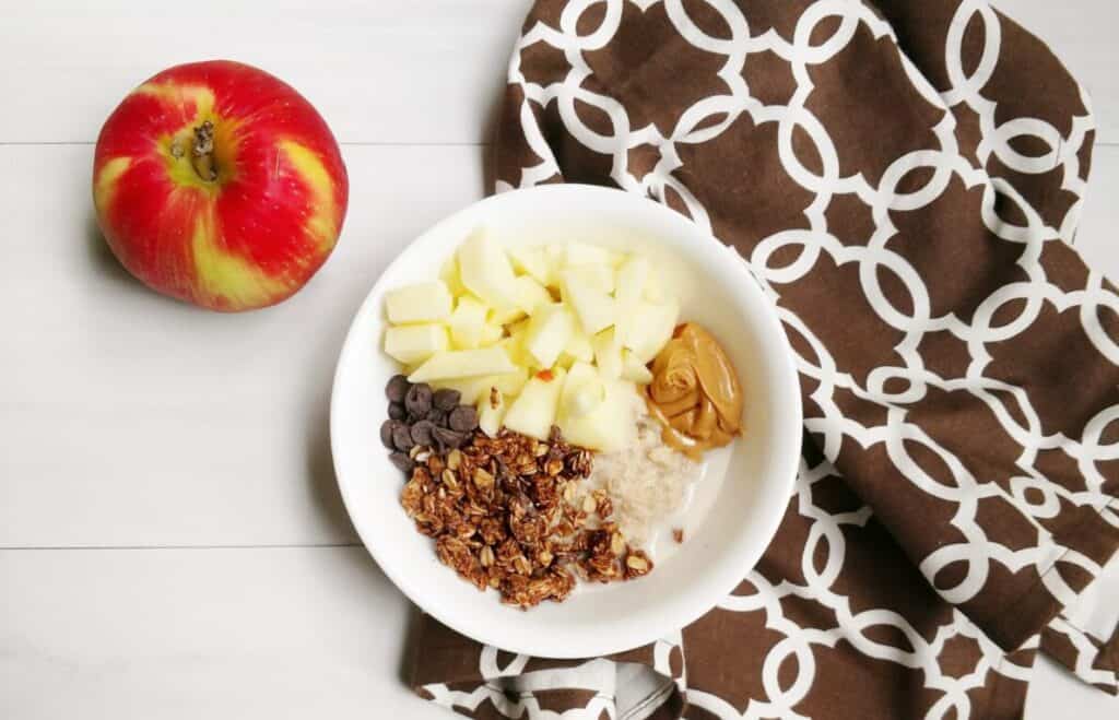 A bowl of oatmeal with apples and peanut butter.